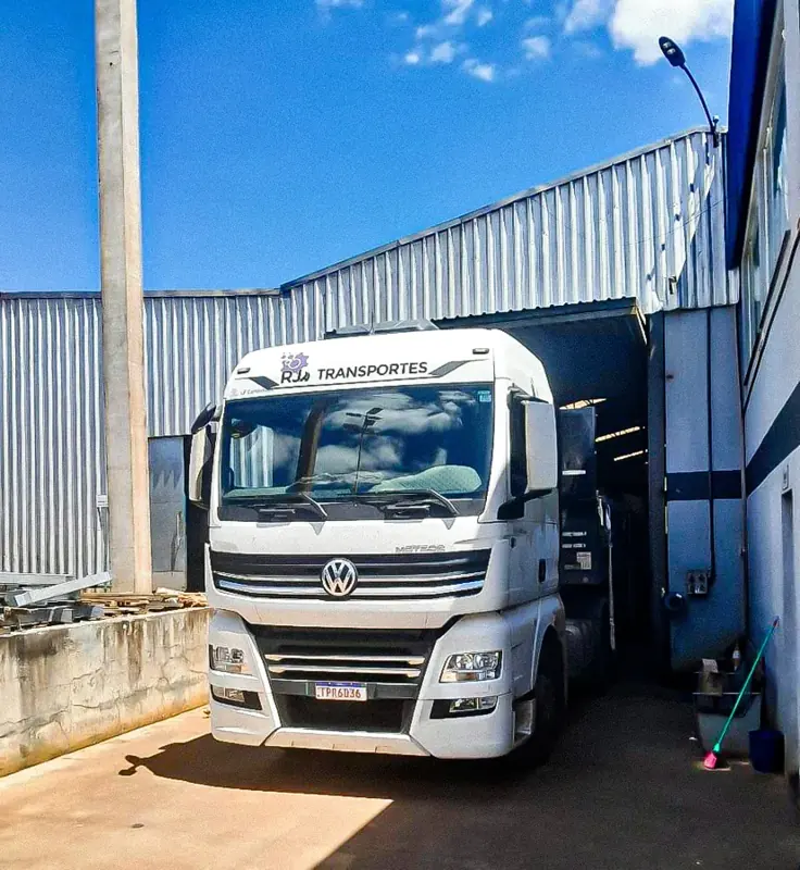 Cavalo mecânico branco da RJ Transportes entrando no galpão da fábrica