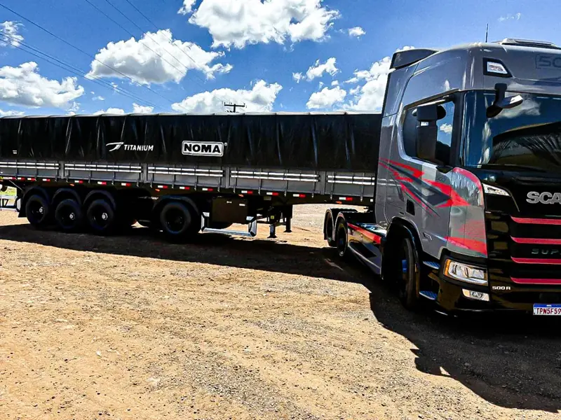 Cavalo mecânico cinza e vermelho com carreta graneleira, vista lateral